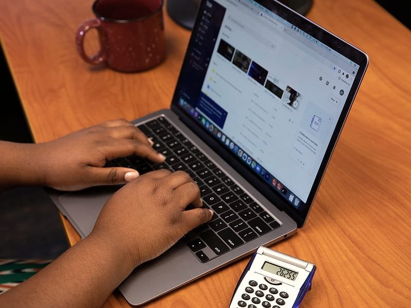 Hands typing on a laptop next to a calculator